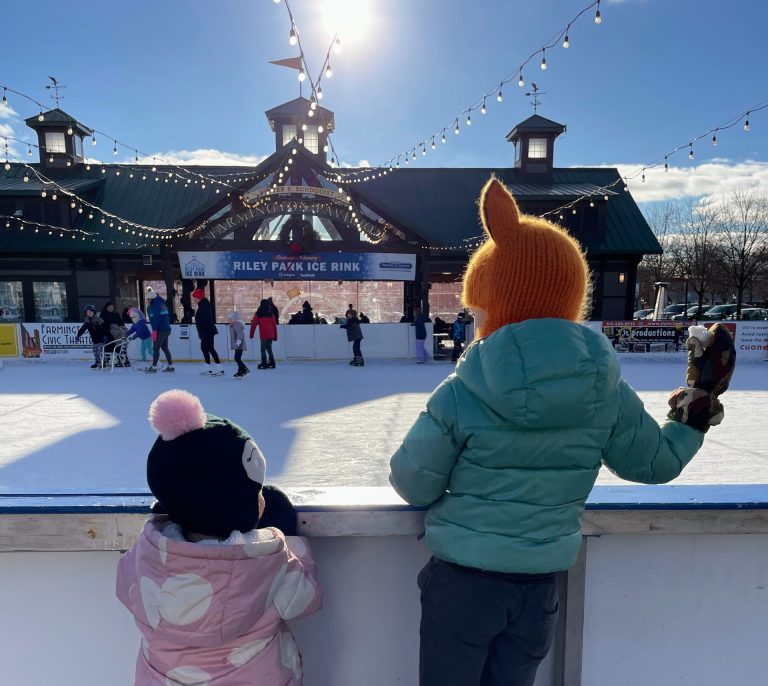 two kids standing next to an ice skating rink in winter on a sunny day